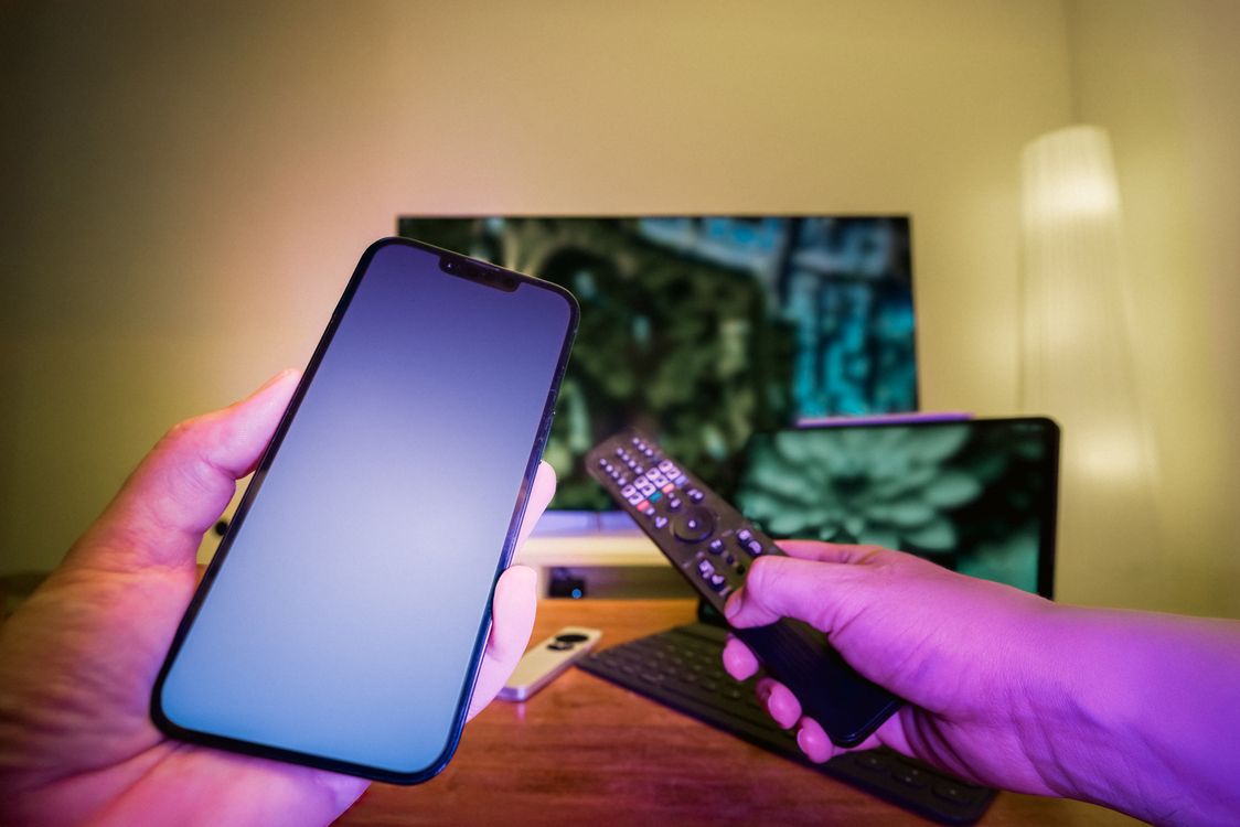 Mains tenant téléphone et télécommande devant Smart TV — configuration IPTV SmartX2 Android TV France